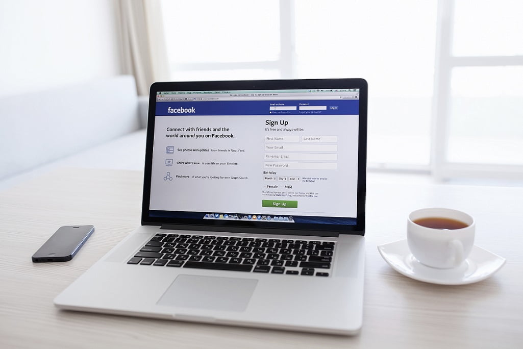 Página de login do Facebook em um notebook entre um iPhone e uma xícara | Novidade no Facebook: anúncios mobile e posts patrocinados